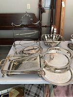 Overall view of the silver plated serving dishes and trays on a table showing the tiered stand, basket bowl, oval platters, and trays.