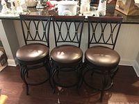 Three metal bar stools with black frames and brown swivel seat cushions, arranged side by side against a kitchen counter.