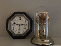 Photo showing both the black octagonal wall clock and the gold-tone glass dome mantle clock side by side.