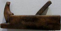 Side view of antique wooden block plane showing forward handle and angled metal blade holder.