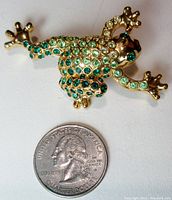 Close-up photo of the gold-tone green leopard frog pin with three peridot shades of rhinestones and a quarter for scale.