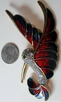 Front view of large hummingbird brooch next to a quarter showing size scale with detailed enamel wings and rhinestone body.