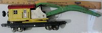 Side profile of Lionel Prewar 810 Crane Car showing yellow crane cab with red roof and green arm mounted on black railcar base
