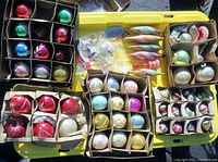 Photo showing multiple boxes of vintage Christmas bulbs with various shapes and colors on a yellow tray.