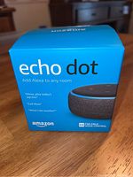 Blue retail box of Amazon Echo Dot showing branding and key phrases about Alexa support and voice control.