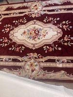 Close-up photo showing rug floral center medallion in burgundy background with detailed flower embroidery.