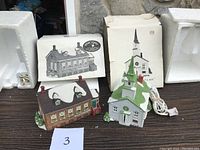 Two Dept 56 New England Village lighted buildings: Stoney Brook Town Hall and Stoney Brook Church displayed on a brown wooden surface with original boxes and white foam packaging visible in background.