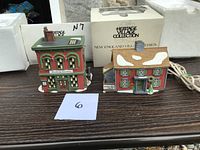 Two Dept 56 New England Village Series porcelain buildings displayed on a table with original box and styrofoam packaging behind them.
