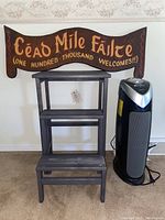 Photo showing dark-stain wooden welcome sign with Irish text above foldable ladder and tower air purifier.