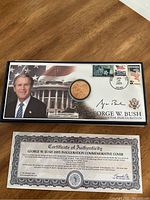 Presentation case showing commemorative coin, George W Bush photo, and inaugural event stamps with postmark dated Jan 20 2005.