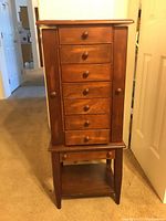 Front view of the wooden jewelry armoire showing six drawers and two side compartments with knobs.