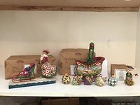 Wide shot showing all Jim Shore figurines and ornaments, including Santa pushing sled, sleigh bell ornaments, and cat ornament, with their boxes behind