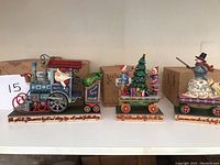Three Jim Shore Christmas-themed train cars on display shelf showing full set including Santa engine, children and tree car, and snowman car with detailed painted designs.
