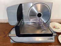 Side view of Cooks brand electric meat slicer showing blade and plastic components