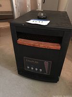 Front view of EdenPURE space heater showing wooden accent handle and control panel with buttons and indicator scale. Remote control on top of the heater.