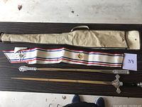 Overview of sword, scabbard, sash and case laid out on table with lot number card visible