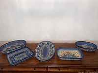 All 5 handmade Polish ceramic trays arranged on a wooden surface, showing shape, size, and colorful painted patterns.