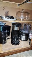 Photo showing Hamilton Beach food processor, OnSly coffee maker, Ilichka coffee grinder, cake plate, plates, and plastic ware stored on a cabinet shelf
