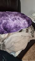 Pile of three blankets stacked on a chair showing top purple faux fur blanket