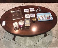 Photo of oval wooden coffee table with the decorative items arranged on top including coasters, candles, XO decor piece, bird tray, brass bowl, and silver bird statues.