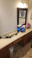 Compound bow on countertop next to packages of toilet tissue and feminine products under wall mirror.