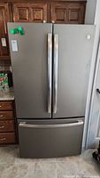 Front view of stainless steel French door refrigerator with bottom freezer drawer installed between wood cabinets.