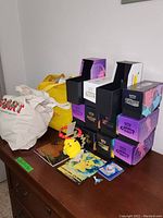 Photo showing stacked Pokemon trading card boxes with two tote bags and a Pikachu figure, packs of cards, player's guide and decal laid out on surface.