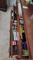 Open wooden drawers showing assorted Pokemon TCG items, cables, binders, tissue paper