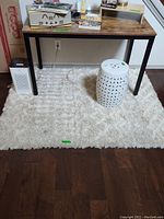 View of textured white and beige area rug under wooden desk with white ceramic stool on top, showing pattern and size