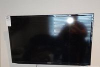 Front view of Samsung flat-screen television with black bezel and screen off, showing sticker on top left corner.