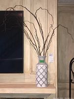 White ceramic vase with lattice pattern containing tall, curly faux branches.