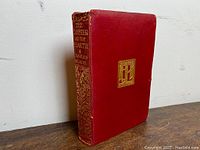 View of the book spine showing gold embossed title and author on red leather binding with visible wear.