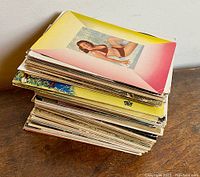Stack of postcard collection with a visible pin-up girl on the top postcard showing vibrant pink and yellow border.