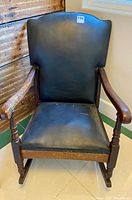 Front view of antique rocking armchair showing black cloth upholstery and wooden armrests.