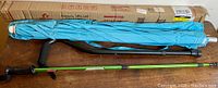 Photo showing the turquoise cotton patio umbrella with aluminum pole next to a Coleman green walking stick and a black cane, all laid out on wooden surface.