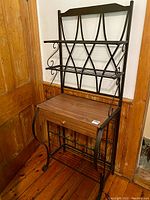 Full view of contemporary bakers rack showing wrought iron frame, wooden drawer shelf, and three metal shelves.