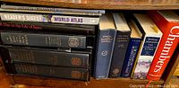 Shelf with unusually large and oversized dictionary volumes, boxed Oxford two-volume set with magnifying glass visible, along with reference books and atlases.