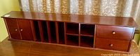Full front view of the darkwood shelf showing 2 doors on left, 5 vertical open compartments, 2 square open compartments, and drawers on right side.