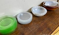 Stacks of green uranium glass dinner plates and clear ribbed glass plates, with several Pyrex bowls behind.