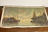 Full view of the unframed oil painting on canvas laid flat showing boats and buildings on water with muted cloudy sky.