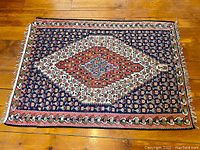 Full view of the hand woven cotton Persian carpet on wood floor showing symmetrical central medallion with floral pattern in dark blue, red, white and green tones.