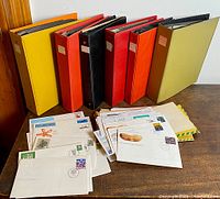 Seven professional albums in assorted colors with large amounts of Canadian First Day Covers, some covers arranged outside the albums on the table.