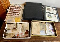 Overall view showing black binder, two boxes with loose stamps and covers, envelopes, and sheets of numerous postage stamps including an intact sheet of stamps.