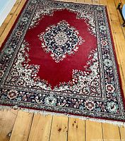 Full view of the vintage Persian style carpet showing red central field with navy medallion and floral borders on hardwood floor.
