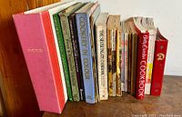 Side view of vintage cookbooks collection with pink photo album and various titles visible.