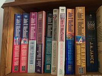 Shelf of 11 John D. MacDonald paperback books and 1 Kiss the Bees book