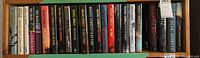 Shelf full of hardcover fiction books, showing spines with multiple authors including Jeffrey Archer, James Lee Burke, Paul Mann, Michael Connelly, and Dean Koontz.