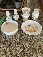 Top view of four porcelain pieces on countertop: two Royal Adderley salt and pepper shakers (white with crest and floral), Aynsley Cottage Garden scalloped bowl, and Aynsley floral plate with butterfly.