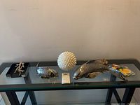 Full view of lot: two metal fish figurines, seashell ball, black metal tray with coral shaped napkin holder