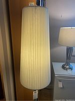 Full view of the tall white pleated shade with visible texture and lamp base partially seen.